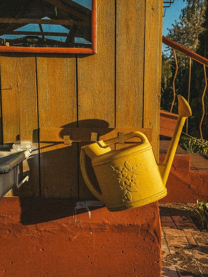 Bright yellow watering can on rustic wooden wall, bathed in warm sunlight.
